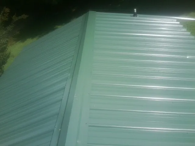 New green metal panels meeting at the ridge of a roof — Flat Roof Repair work by our crew in Nederland